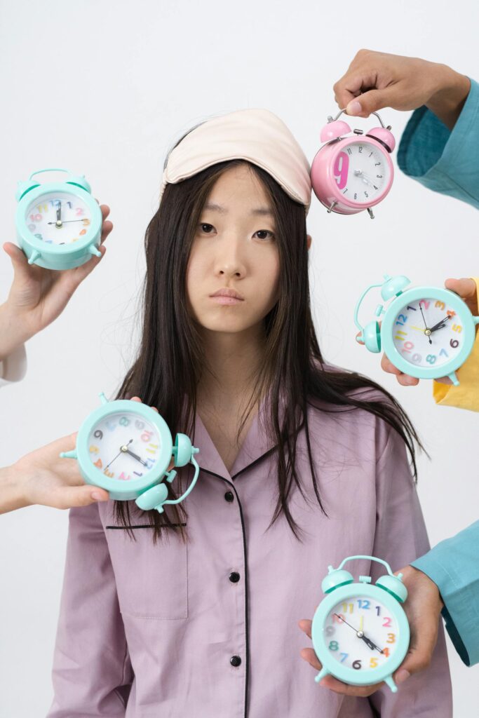 Asian woman in pajamas with alarm clocks, illustrating insomnia concept.
